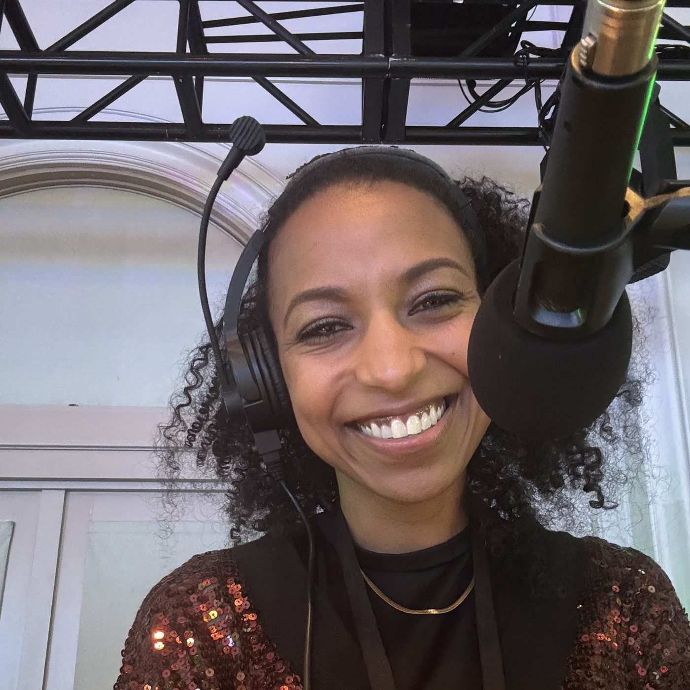 Chelsea smiling on headset at the Live Voice MC booth in a sequin jacket