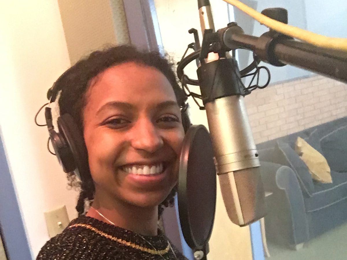 Chelsea smiling at the mic in a voiceover recording booth